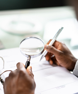 Magnifying glass with hands holding a pen.